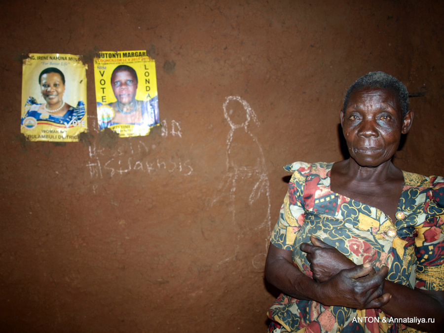 Женщина внутри своего дома. На стене висят предвыборные плакаты Уганда