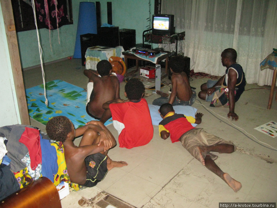 В цивильном доме золотодобытчика Алекса Данти дети смотрят телевизор (от генератора) Варомо, Папуа-Новая Гвинея