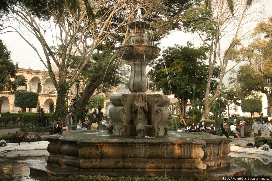 Фонтан на центральной площади. В основании фонтана — женщина. закрывающая грудь руками Антигуа, Гватемала