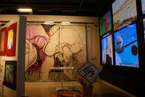 Около стены вертикально повешены три больших экрана, на которых транслируются ролики и реклама.