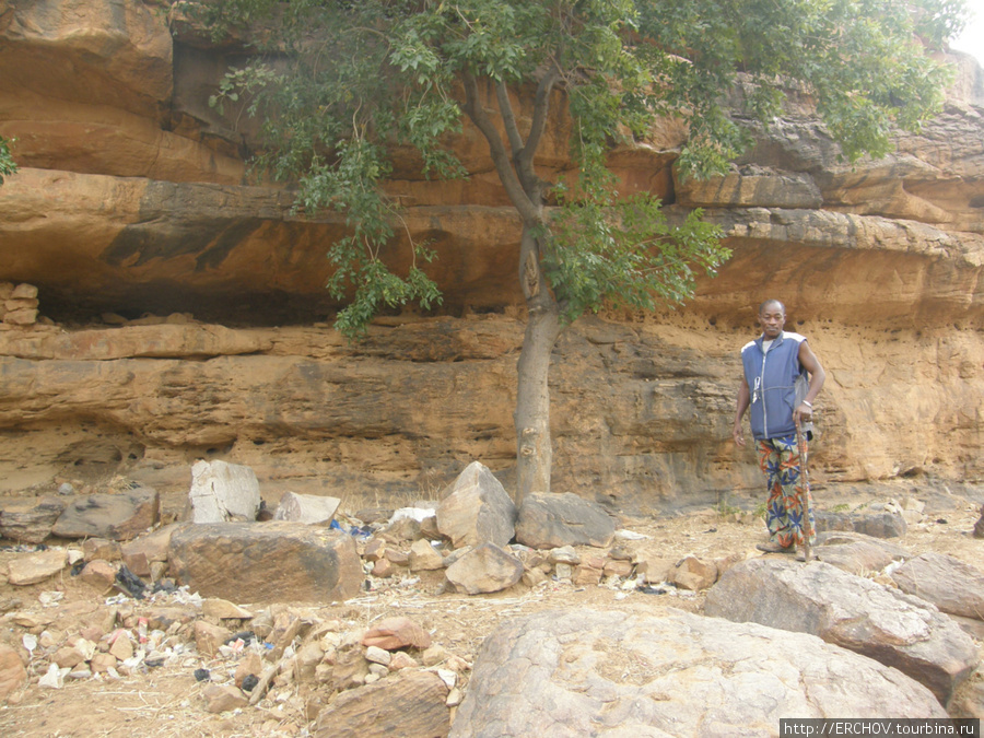 За спиной гида священные расщелины в скале. Область Мопти, Мали
