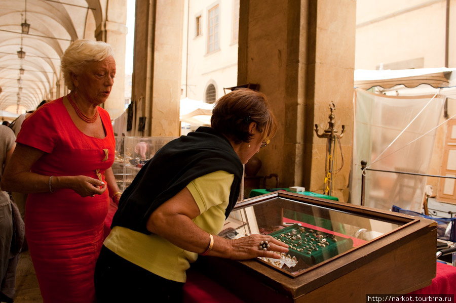 Эта женщина (в красном) продает на рынке дольше 20 лет. Продает старинные золотые украшения, некоторые можно купить по отличной цене. Выписывает справку о покупке и дает свой адрес, очень чистая репутация и серьезное отношение к делу  .(под портиком) Ареццо, Италия