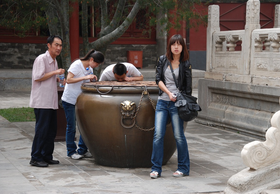 Люди кидают монетки через квадратное отверстие вверху и стараются попасть в небольшую чашу на дне. Пекин, Китай